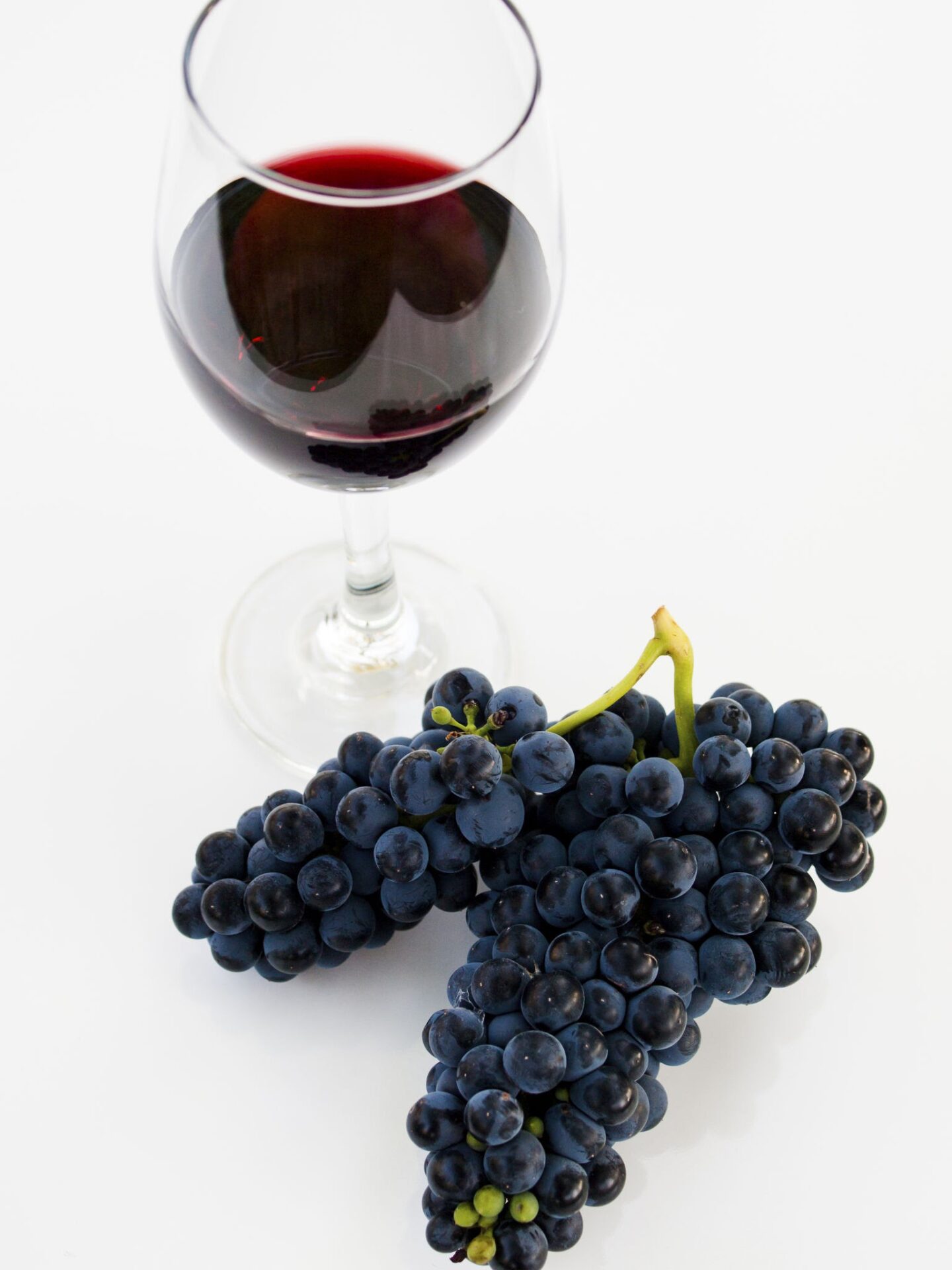 Grapes and red wine in glass on white backgound.