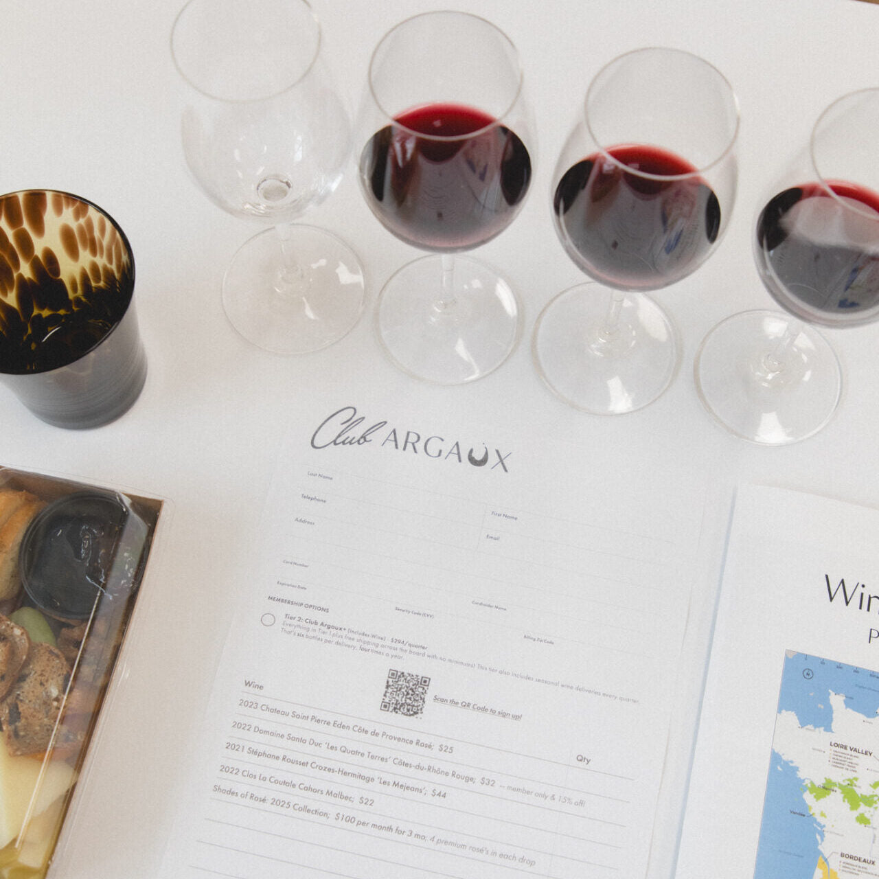 Wine glasses with red wine on a table with 'Club Argaux' menu and map.