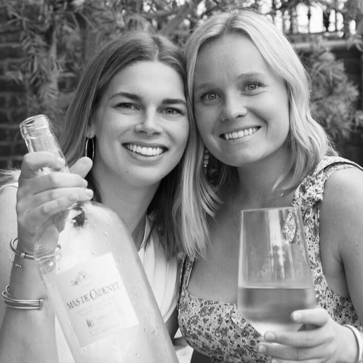 Two women holding bottles of wine outdoors