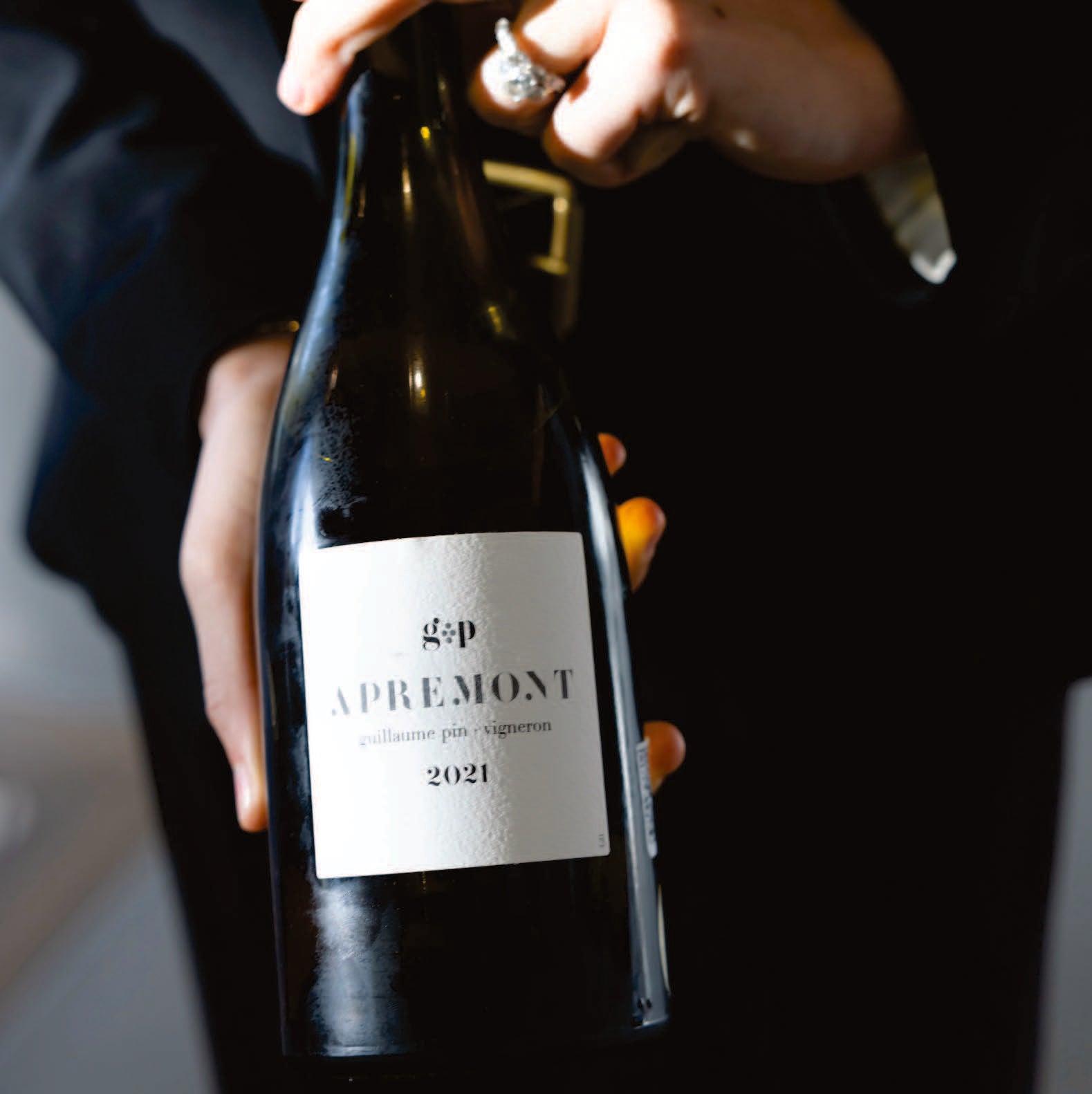 Person holding a wine bottle labeled 'gép Apremont 2021' with a blurred background