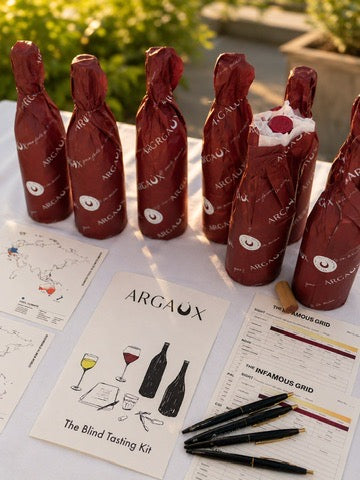 Argaux wine bottles wrapped in packaging for blind wine tasting kit materials on a table outdoors.