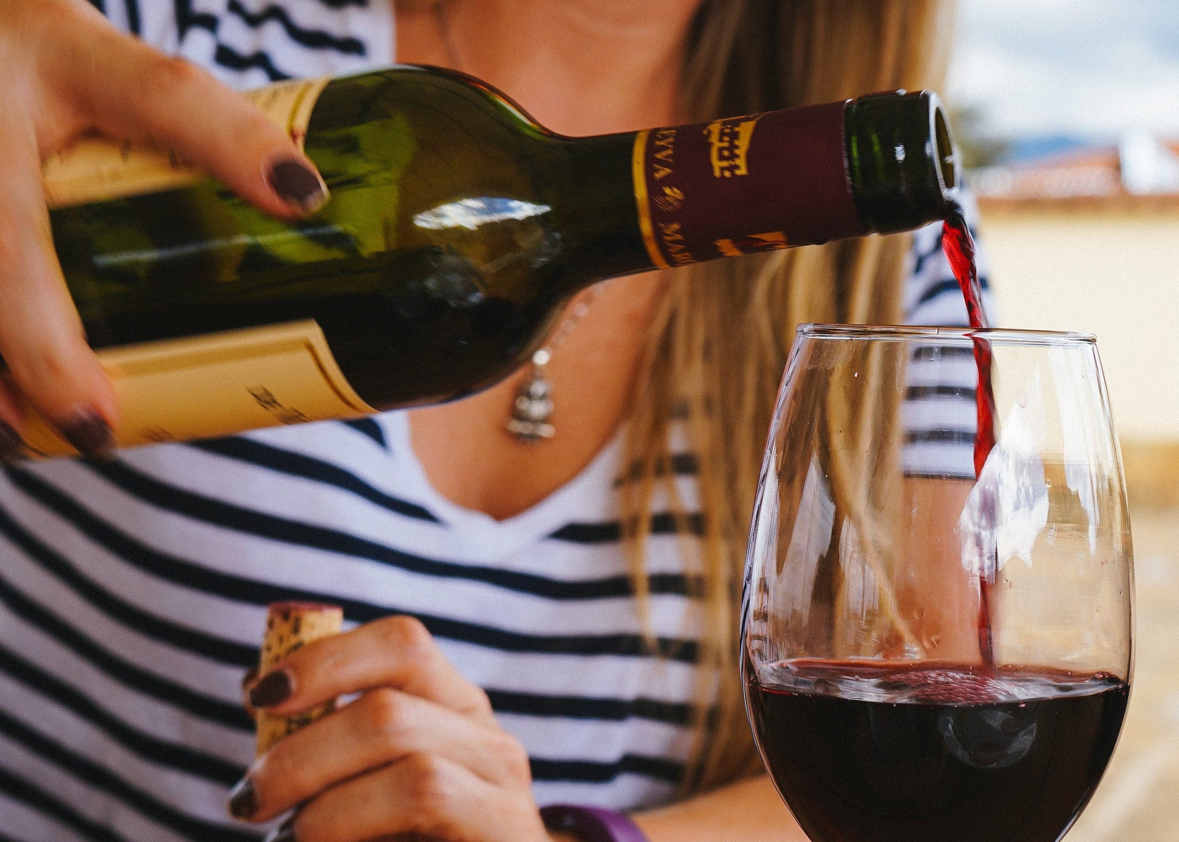 Person pouring red wine into a glass outdoors